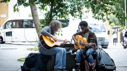 image show two people playing guitars whilst sat under a tree