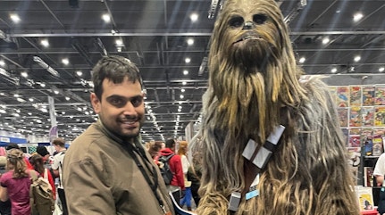 Image shows young man smiling whilst posing with a character in costume at Comic Con