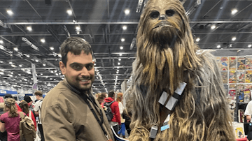 Image shows young man smiling whilst posing with a character in costume at Comic Con