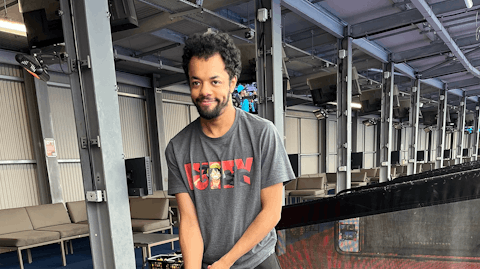 Image shows Casey smiling at the camera whilst taking a swing with a golf club